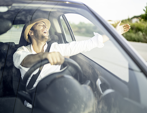 IMAGE: Man driving car with hand out window, singing.