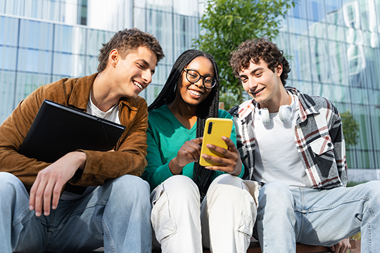 IMAGE: Young adult friends looking together at a phone smiling
