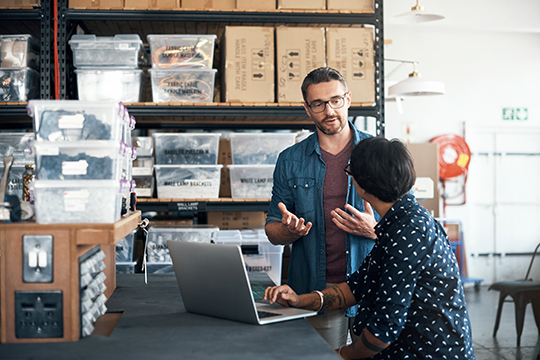 IMAGE: Coworkers talking inside store room with laptop open