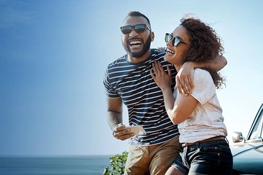 IMAGE: Couple laughing while sitting on the hood of a car