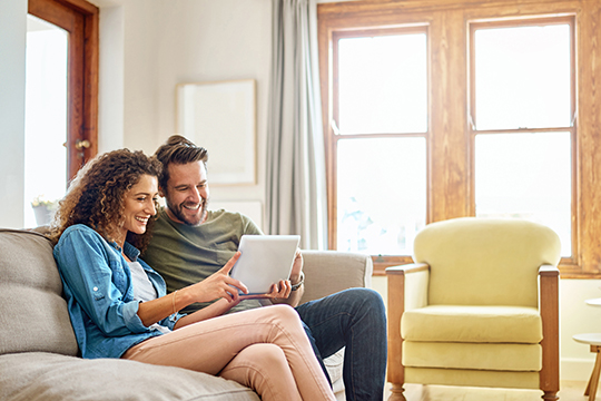 IMAGE: Couple sitting on a couch and holding tablet smiling