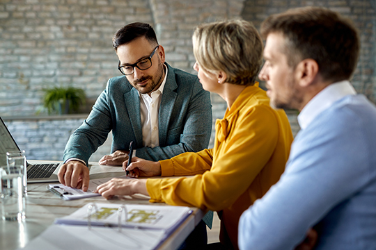IMAGE: Couple talking with real estate agent and signing paperwork