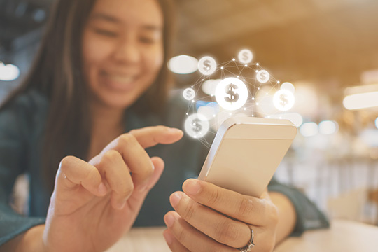 IMAGE: Woman holding phone and about to touch screen with dollar sign icons floating above the phone