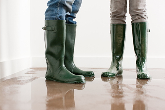 IMAGE: Two people standing in rain boots inside flooded house