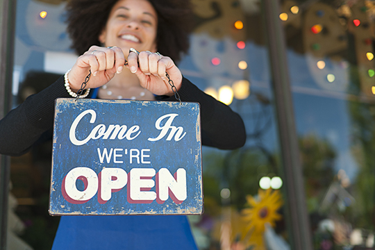 IMAGE: Woman holding a sign that says Come In We're Open
