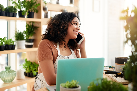 IMAGE: Woman talking on phone and smiling while working in plant shop.