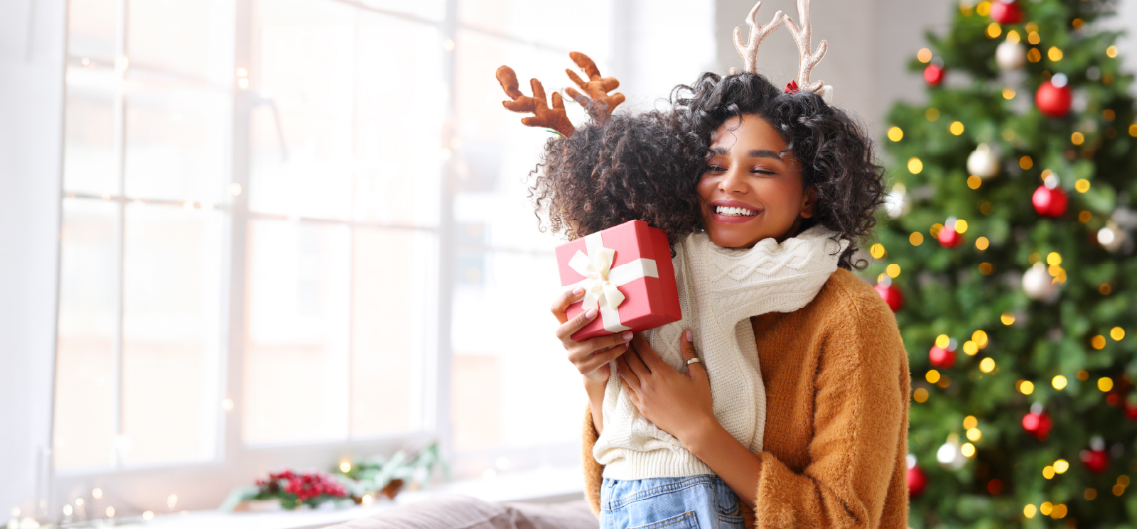 IMAGE: Mom hugging kid with gift in hand in front of Christmas tree