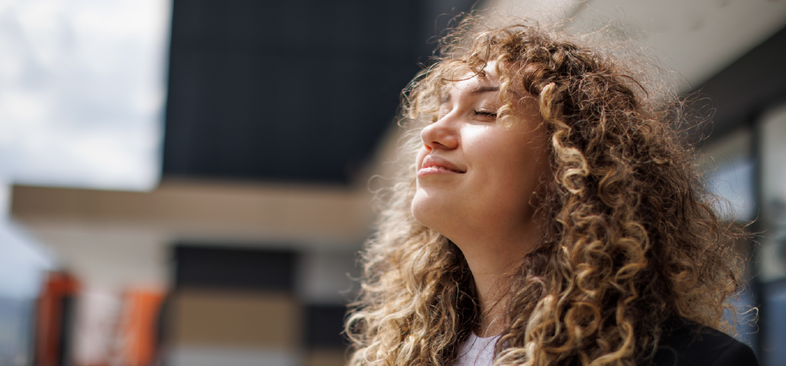 IMAGE: Woman smiling with eyes closed outside building