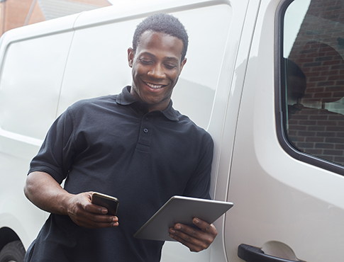 IMAGE: Man holding phone and tablet leaning against a commercial van