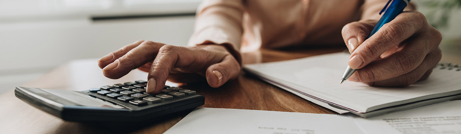 IMAGE: Close view of one hand on calculator and the other writing in a notepad.